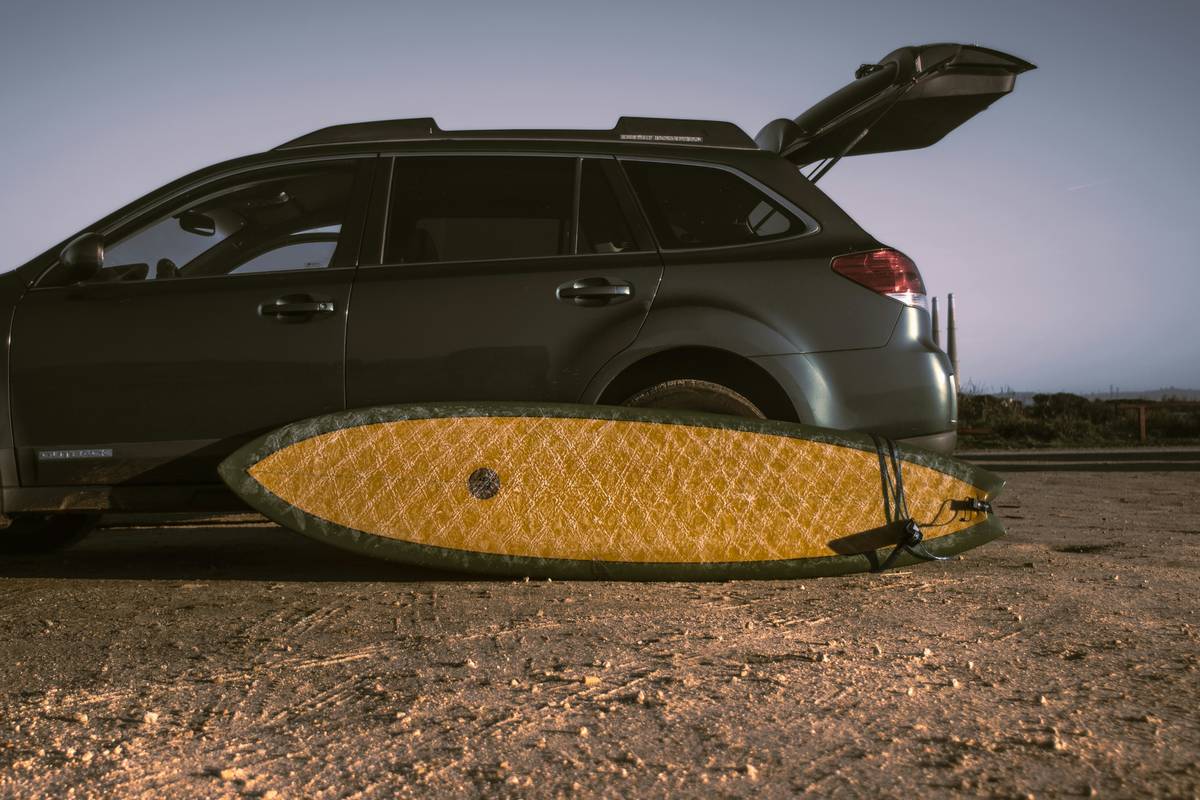 Black surfboard travel bag with wheels, fully zipped and strapped, sitting upright on airport tarmac with visible padding and rugged exterior
