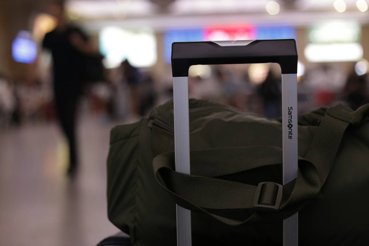A surfer loading a hard-shell surfing and surfboard travel cases into an airport luggage cart